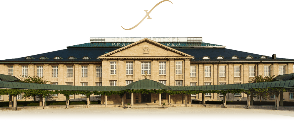 Large beige building with a peak and mansard roof. There is a colonnade with a green awning protecting a covered walkway across the front.