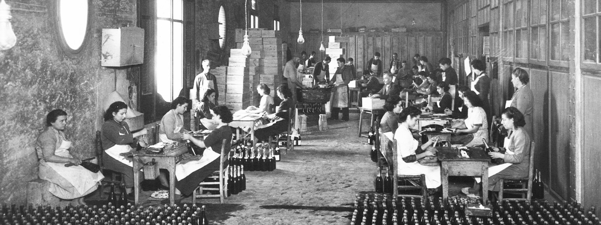 Early Freixenet female employees applying labels to bottles in a large room.